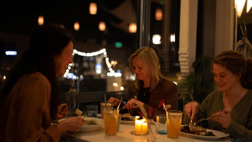 tre personer spiser på restaurant med vinterbelysning ute og inne
