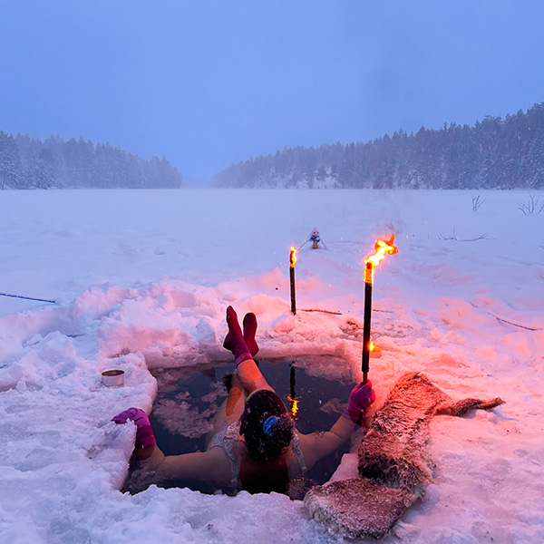 Person bader i hull i isen med fakler rundt
