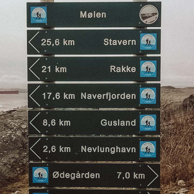 Veiskilt som viser avstander langs kyststien. Skiltet viser retning og kilometer til Mølen, Stavern, Rakke, Naverfjorden, Gusland og Nevlunghavn.