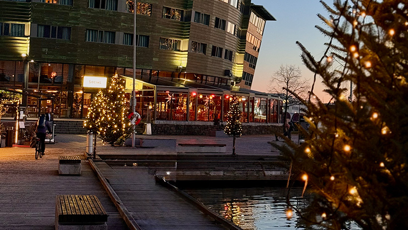 Julelys på bygning ved sjøen og juletre med belysning på brygge